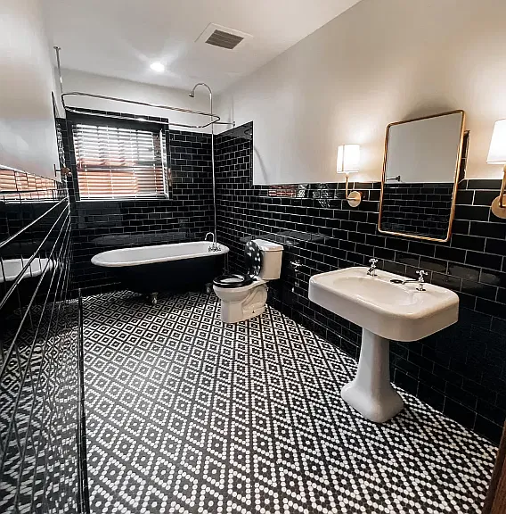 Bathroom with black subway tile walls, a clawfoot tub, a pedestal sink and black-and-white patterned floor tile
