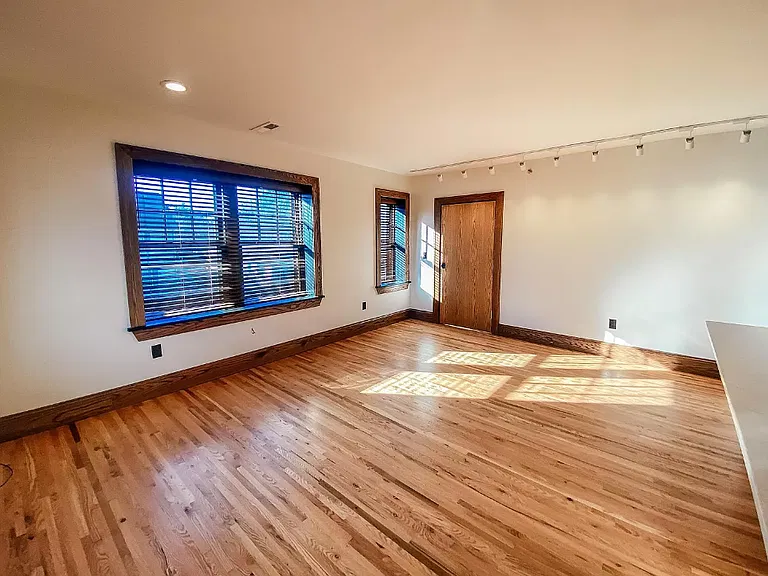 Bright living room with hardwood floors, large windows with blinds and track lighting