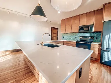 Kitchen with a white quartz island, wood cabinets, green tile backsplash and a pendant light